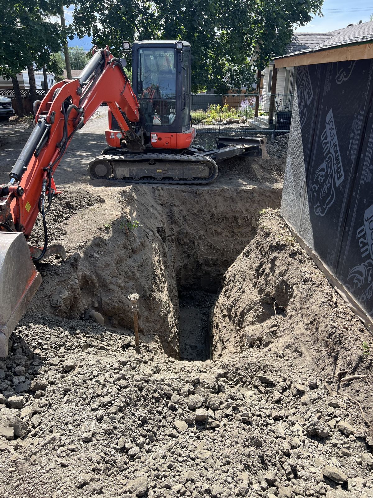 Excavator digging a deep footing trench beside a new build