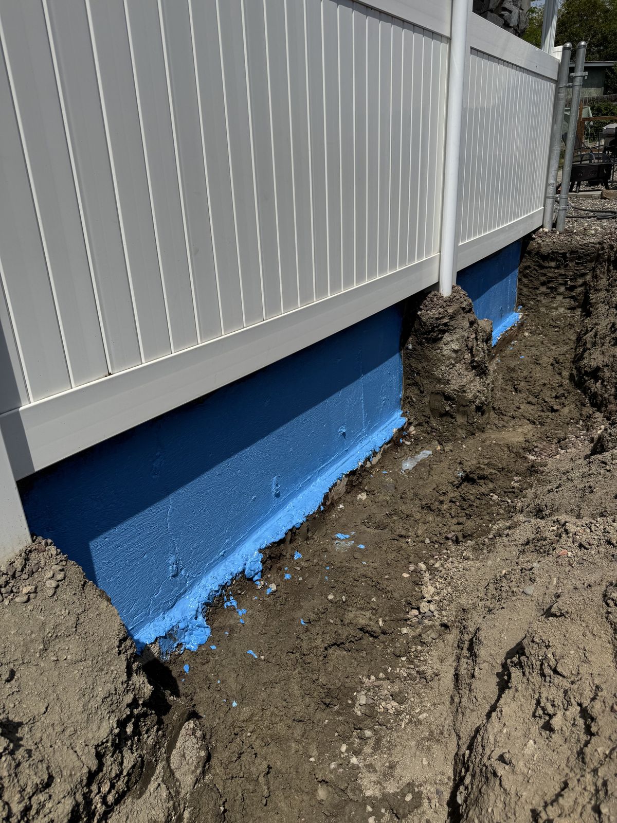 Foundation wall waterproofed with blue membrane, drain trench ready for backfill